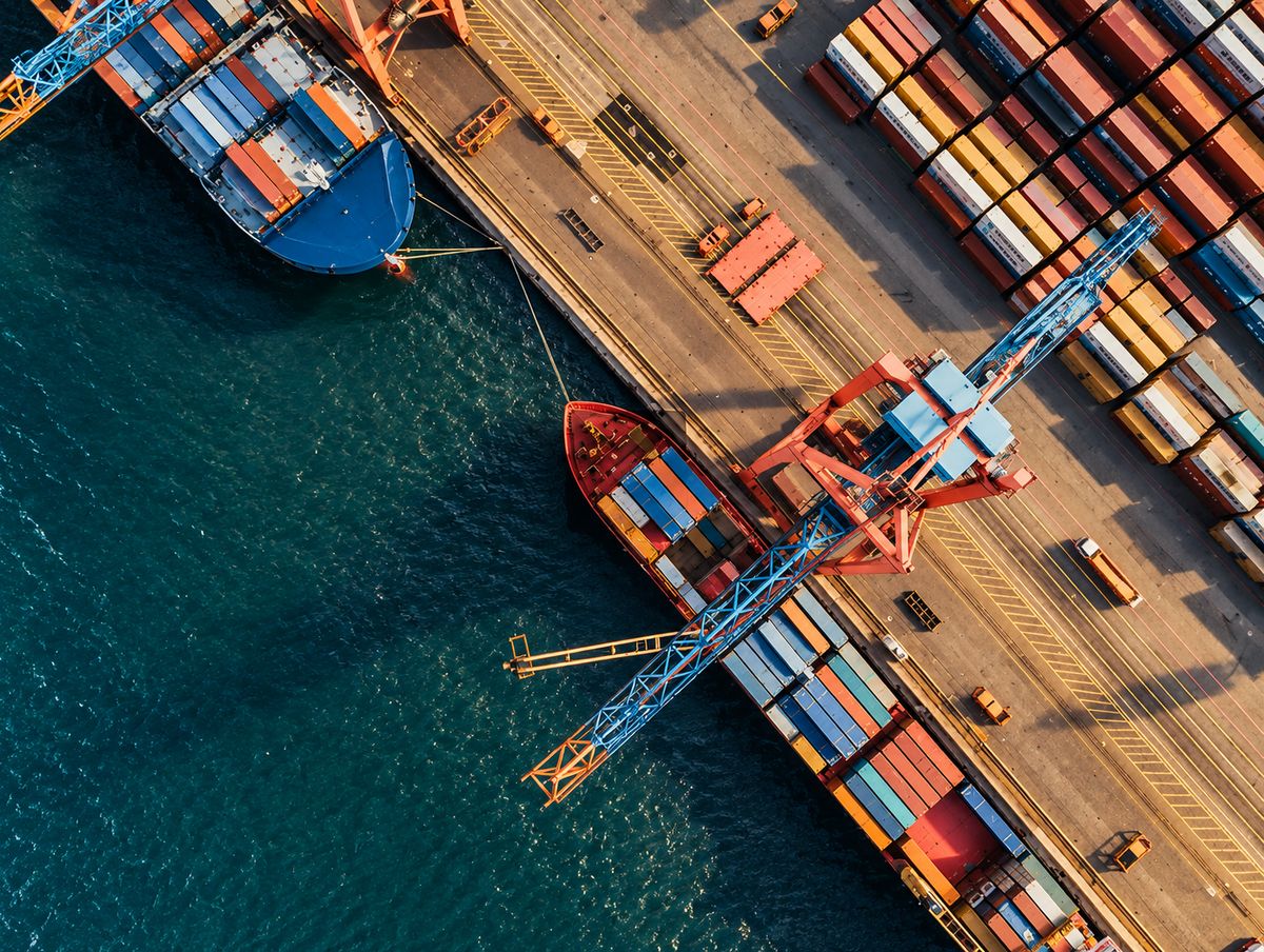 Vista aérea de una terminal portuaria con buque portacontenedores, grúas y contenedores apilados
